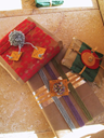 Paper bag wraps the gift. Aluminum foil encircles it. Yarn and raffia bind it. The tag is secured with a pom-pom.